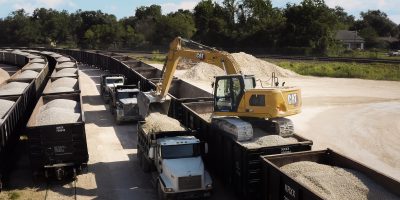 Excavator positioned on train car, loading material into trailer.