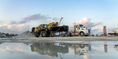 Front loader dumping into trailer, with a puddle reflecting the scene.