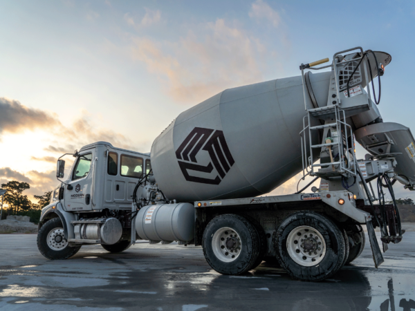 Cement mixer drum truck at sunset, with puddle reflecting the scene.