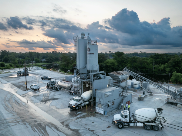 Ready mix concrete plant with several machines visible, including cement mixer trucks and pickup trucks.