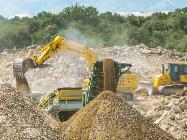 A group a machines on the job, with an excavator harvesting aggregates and a dozer leveling the surface.